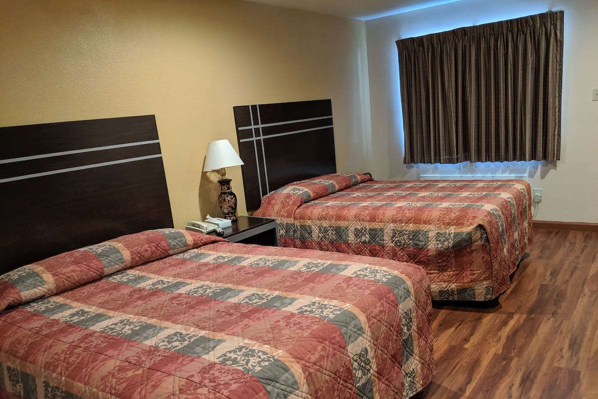 A hotel room with two beds, a nightstand with a lamp, a telephone, and a window with curtains.