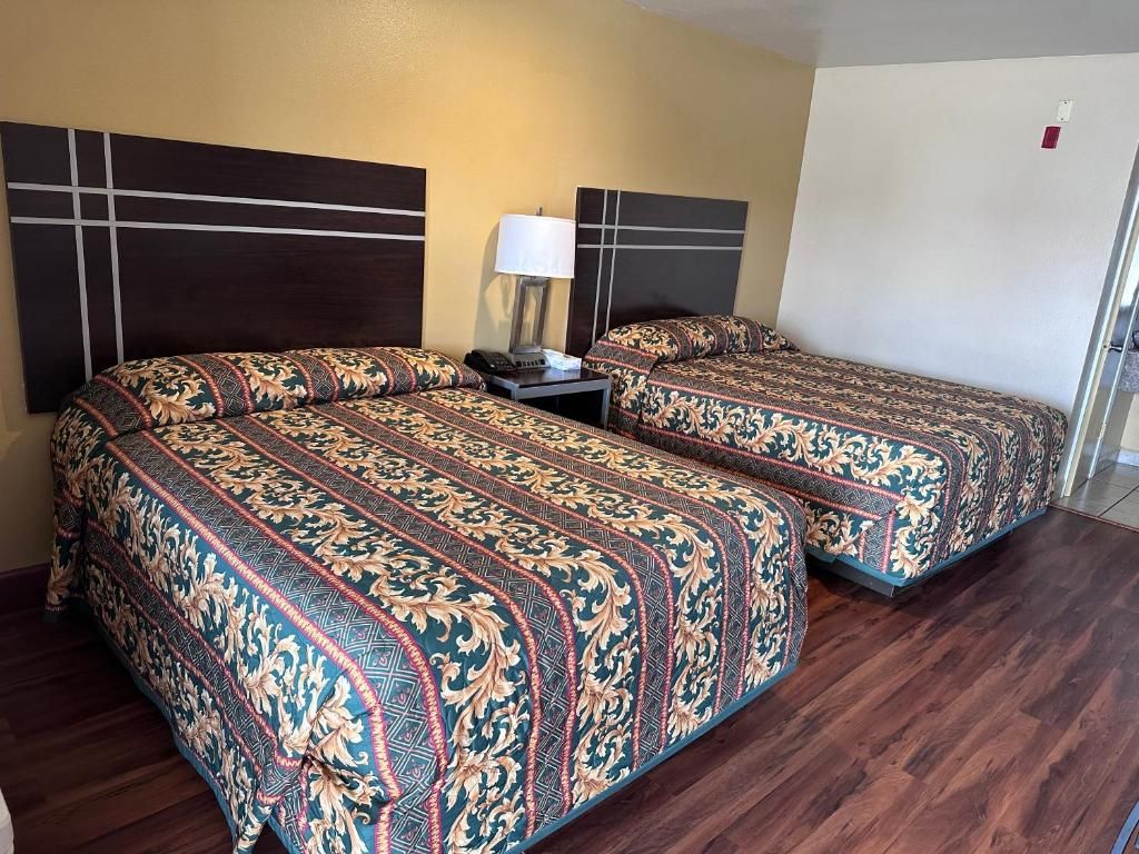 A hotel room with two beds, a nightstand, a lamp, and a door.
