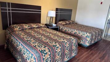 A hotel room with two beds, a nightstand, a lamp, and a door.