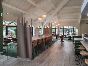 Un restaurante espacioso con techos altos, vigas de madera y amplias ventanas que ofrecen vistas al exterior.