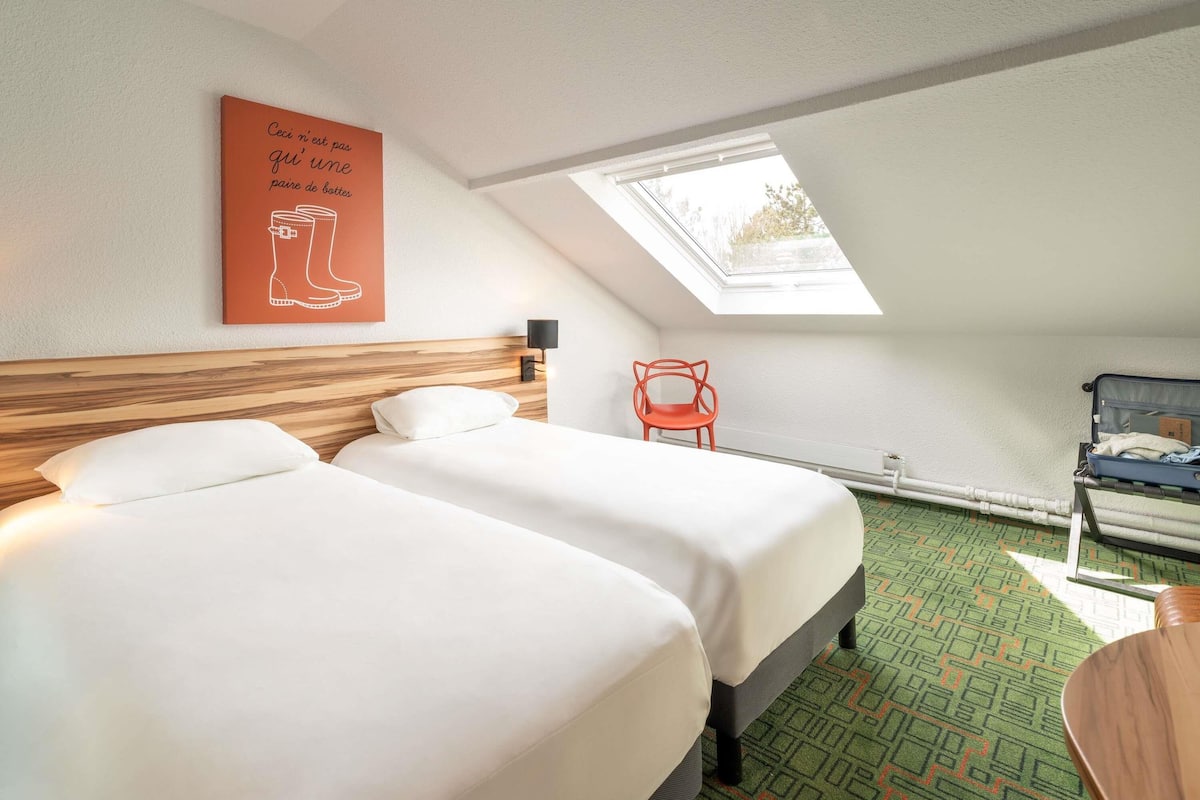 A hotel room with two beds, a skylight, a red chair, and a suitcase on a table.