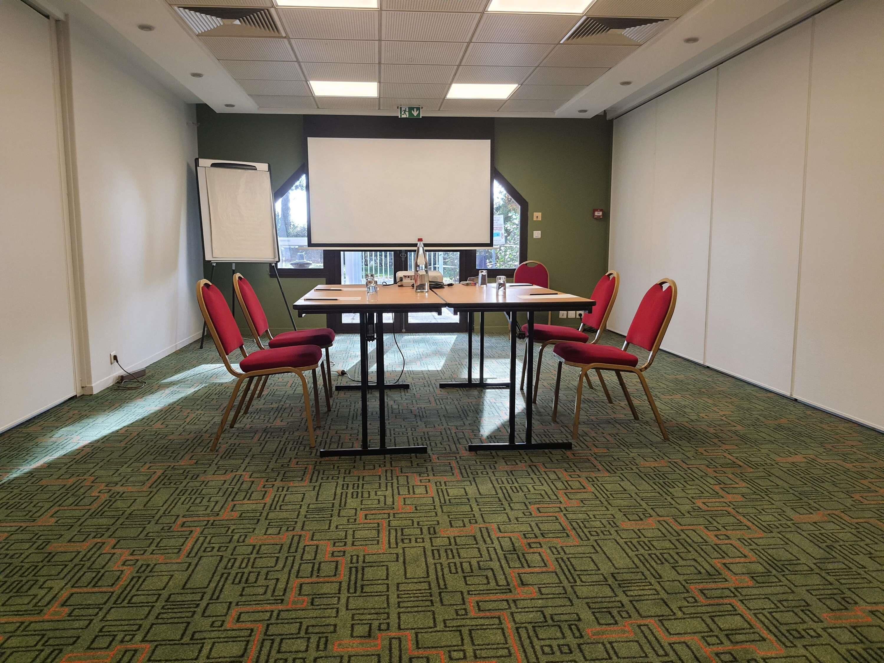 A conference room with a large table, red chairs, a projector screen, and a patterned carpet.
