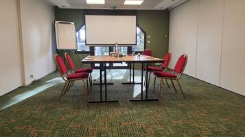 A conference room with a large table, red chairs, a projector screen, and a patterned carpet.