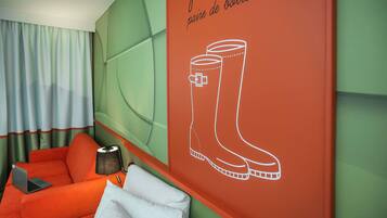 A modern room with a green and orange color scheme, featuring a sofa, a laptop, and a wall with a boot illustration.
