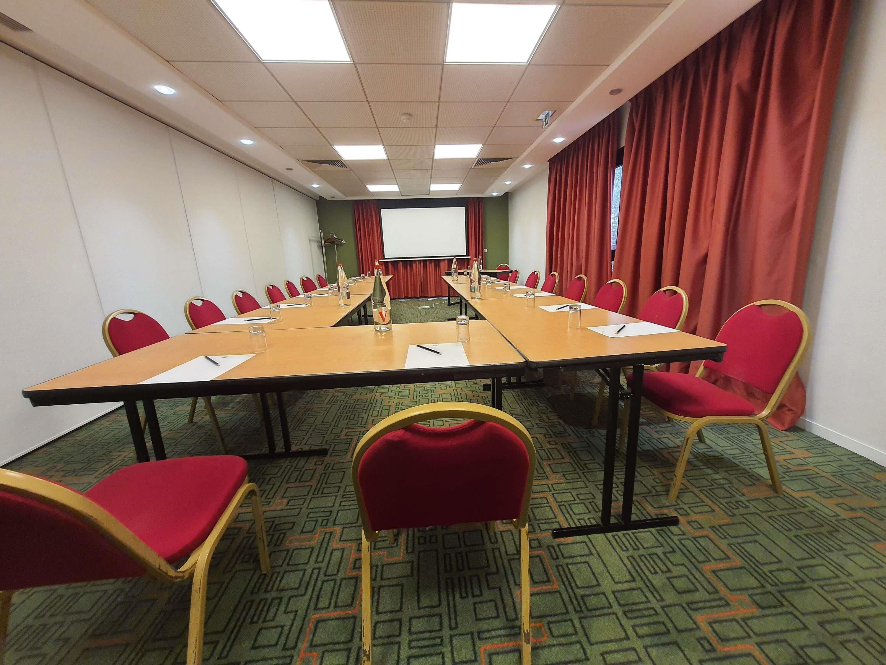 A conference room with a long table, red chairs, a projector screen, and a carpeted floor.