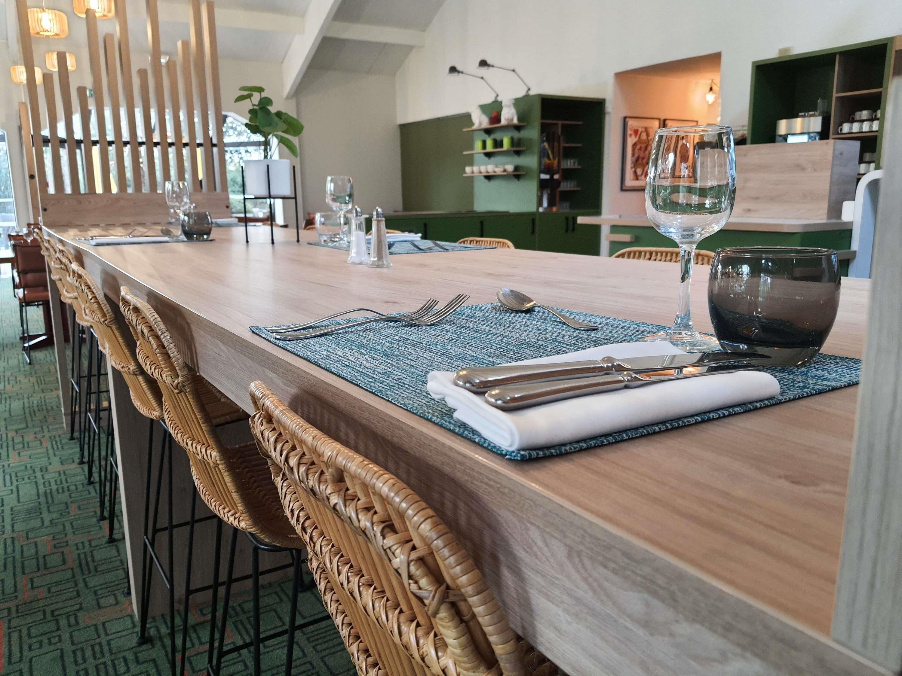 A dining area with a wooden table set for two, including cutlery, a glass, and a napkin.