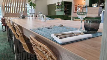 A dining area with a wooden table set for two, including cutlery, a glass, and a napkin.