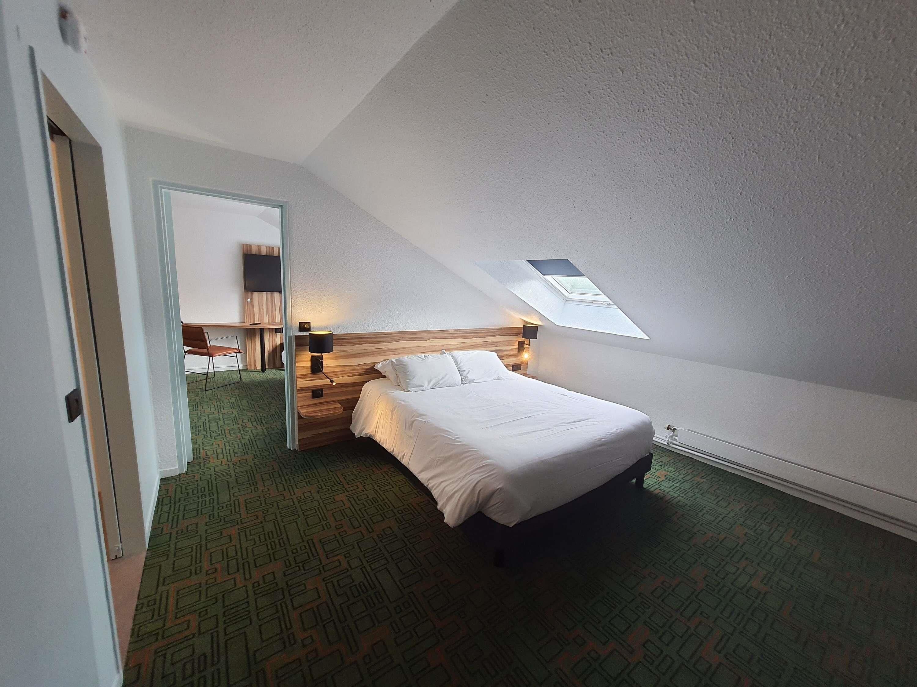 A bedroom with a bed, a desk, a chair, and a skylight.