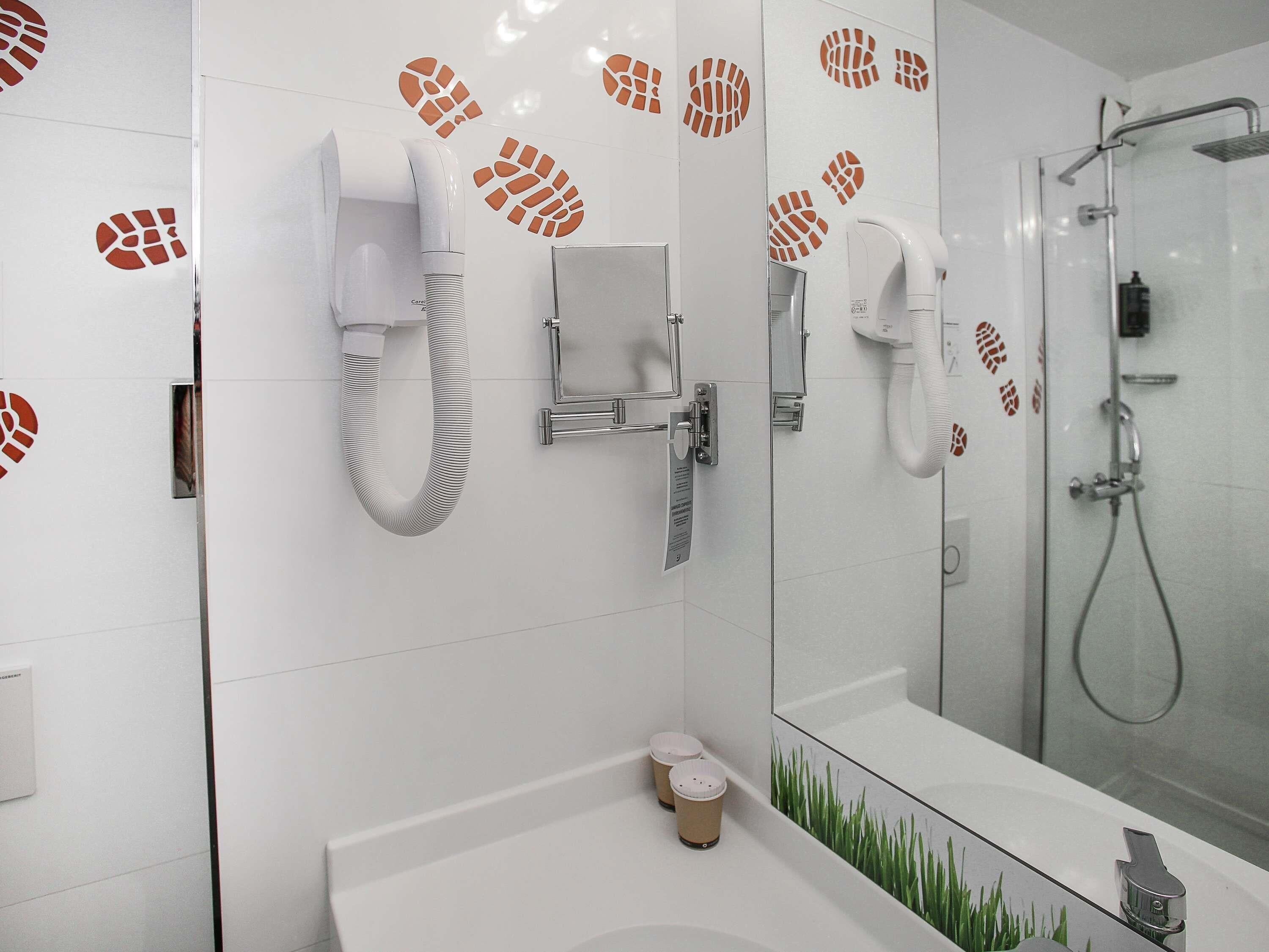 A modern bathroom with a white sink, two hair dryers, a mirror, and a glass shower enclosure.