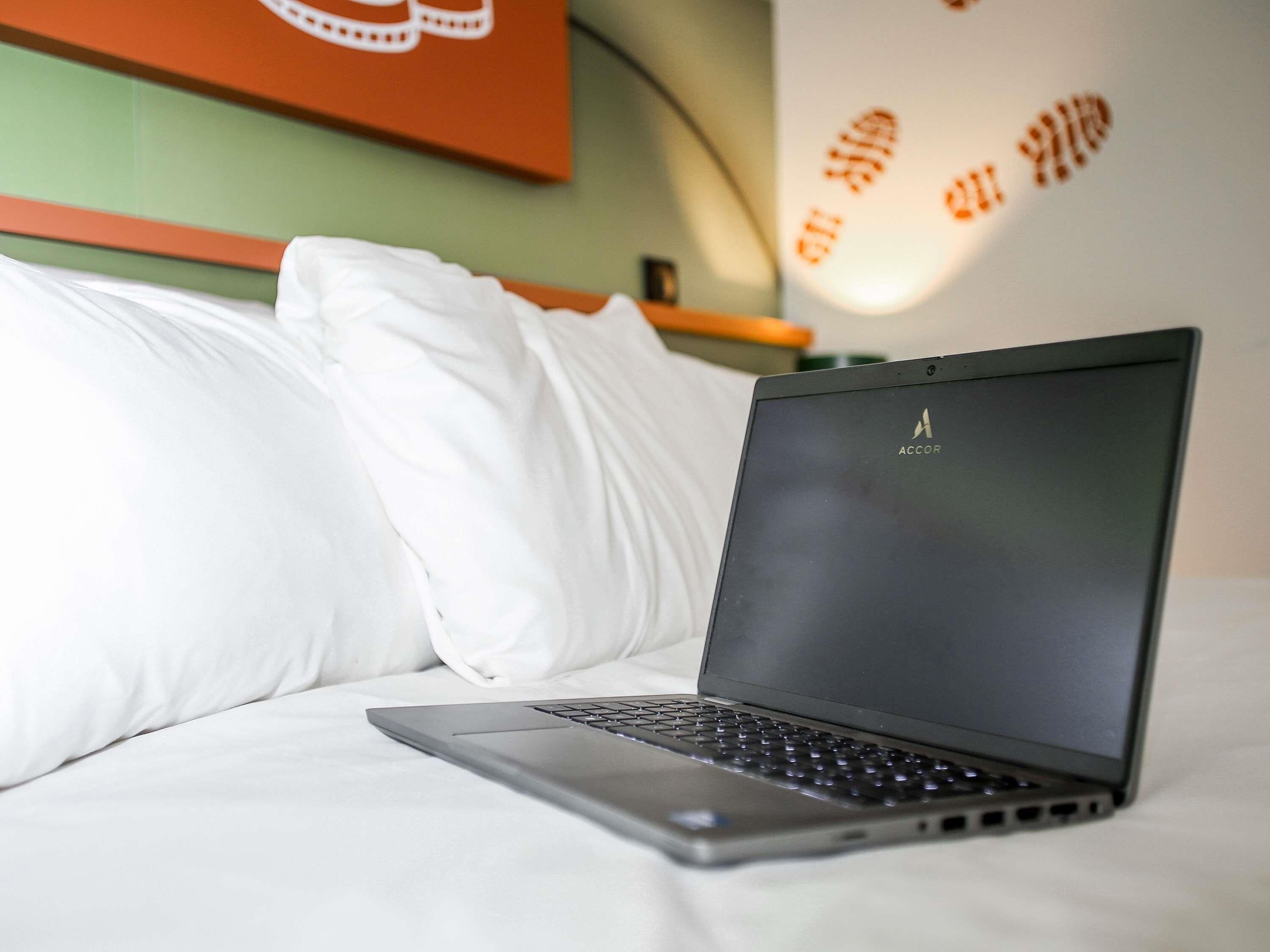 A laptop on a bed with white bedding, a green wall, and a red wall with footprints.