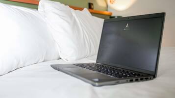 A laptop on a bed with white bedding, a green wall, and a red wall with footprints.
