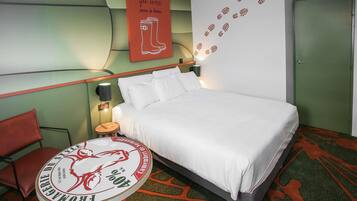 Hotelkamer met een bed, nachtkastje, lamp, stoel en een muur met schoenafdruk decoratie.