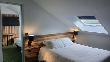 Un dormitorio con techo inclinado, tragaluz, cama con ropa de cama blanca, cabecero de madera y televisor montado en la pared.