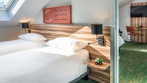 Hotelkamer met een bed, twee bedlampjes, een houten hoofdeinde, een klein tafeltje met een speeltje en een aan de muur bevestigde televisie.