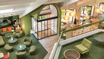 Un hall d’hôtel avec une moquette verte, plusieurs espaces aménagés pour s’asseoir et un escalier menant à un étage supérieur.