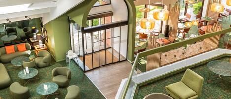 A hotel lobby with a green carpet, multiple seating areas, and a staircase leading to an upper level.