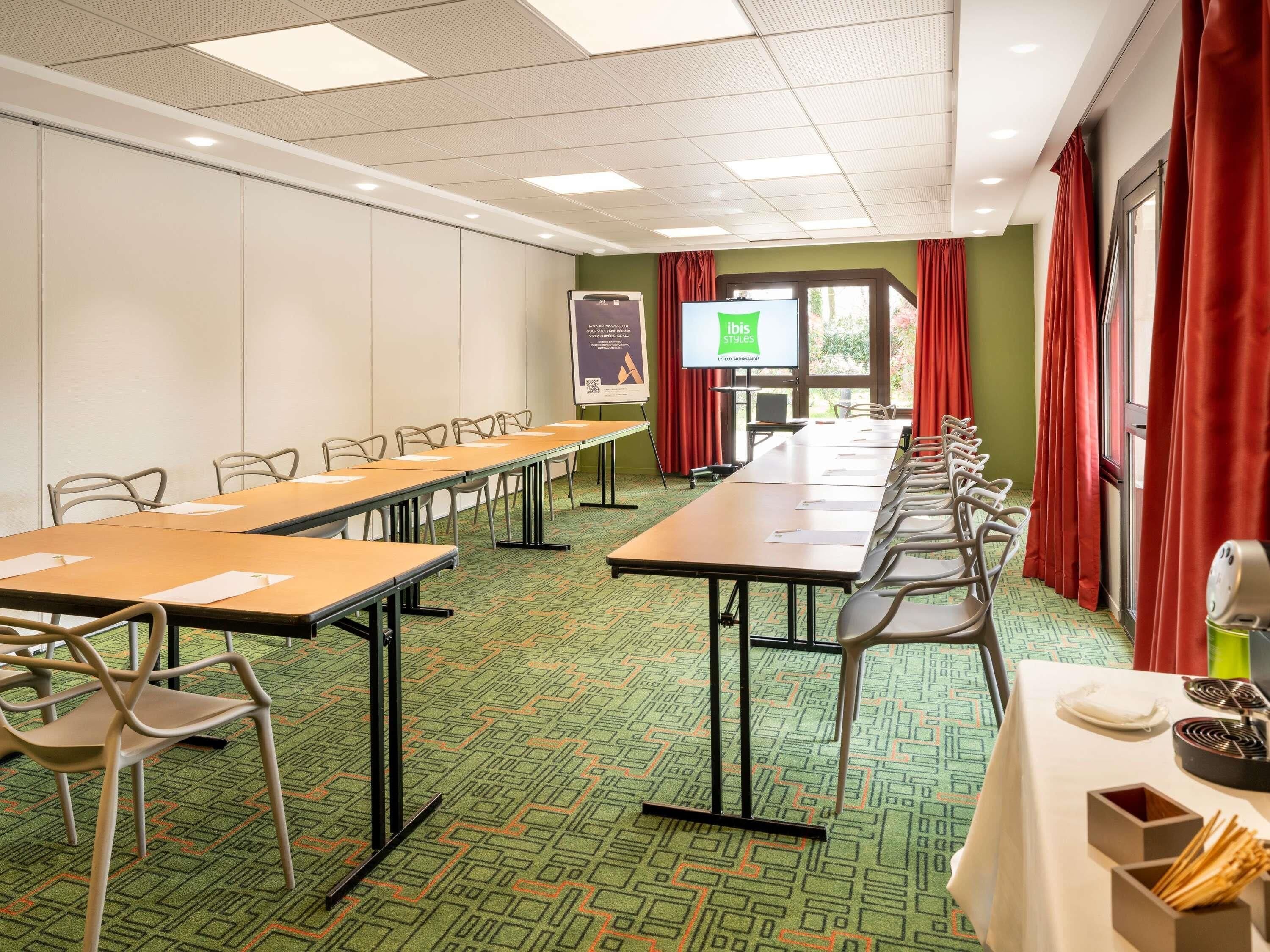Een vergaderzaal met lange tafels, stoelen, een projectiescherm en een presentatie op de muur.
