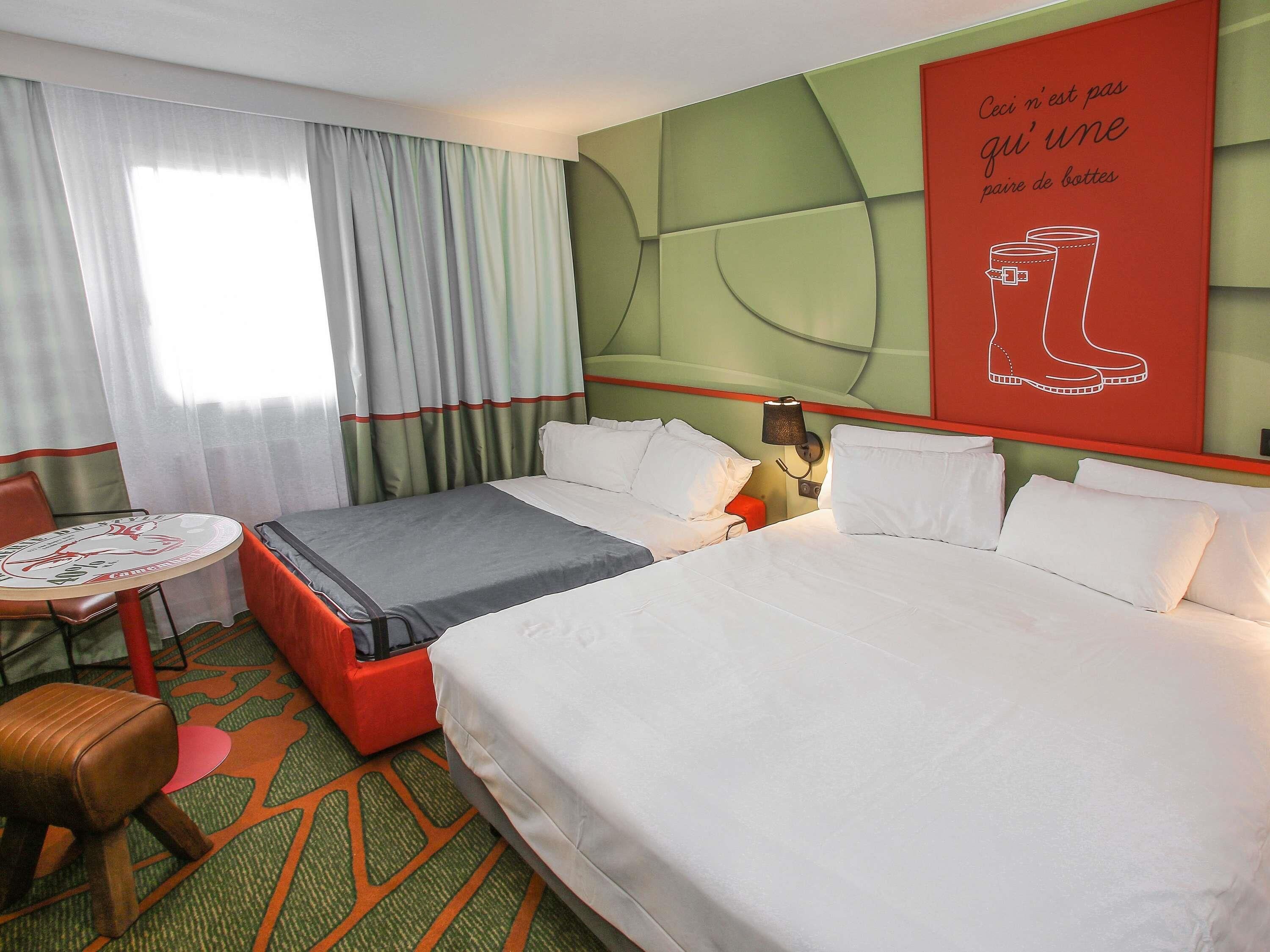 A hotel room with two beds, a small table, a chair, and a wall with a red sign.