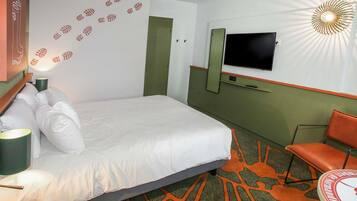 A hotel room with a bed, a TV mounted on the wall, a chair, and a patterned carpet.