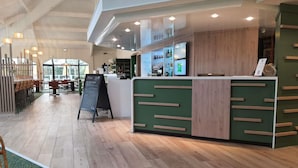 Een moderne receptie met een houten balie, een krijtbordmenu en een zithoek met tafels en stoelen.