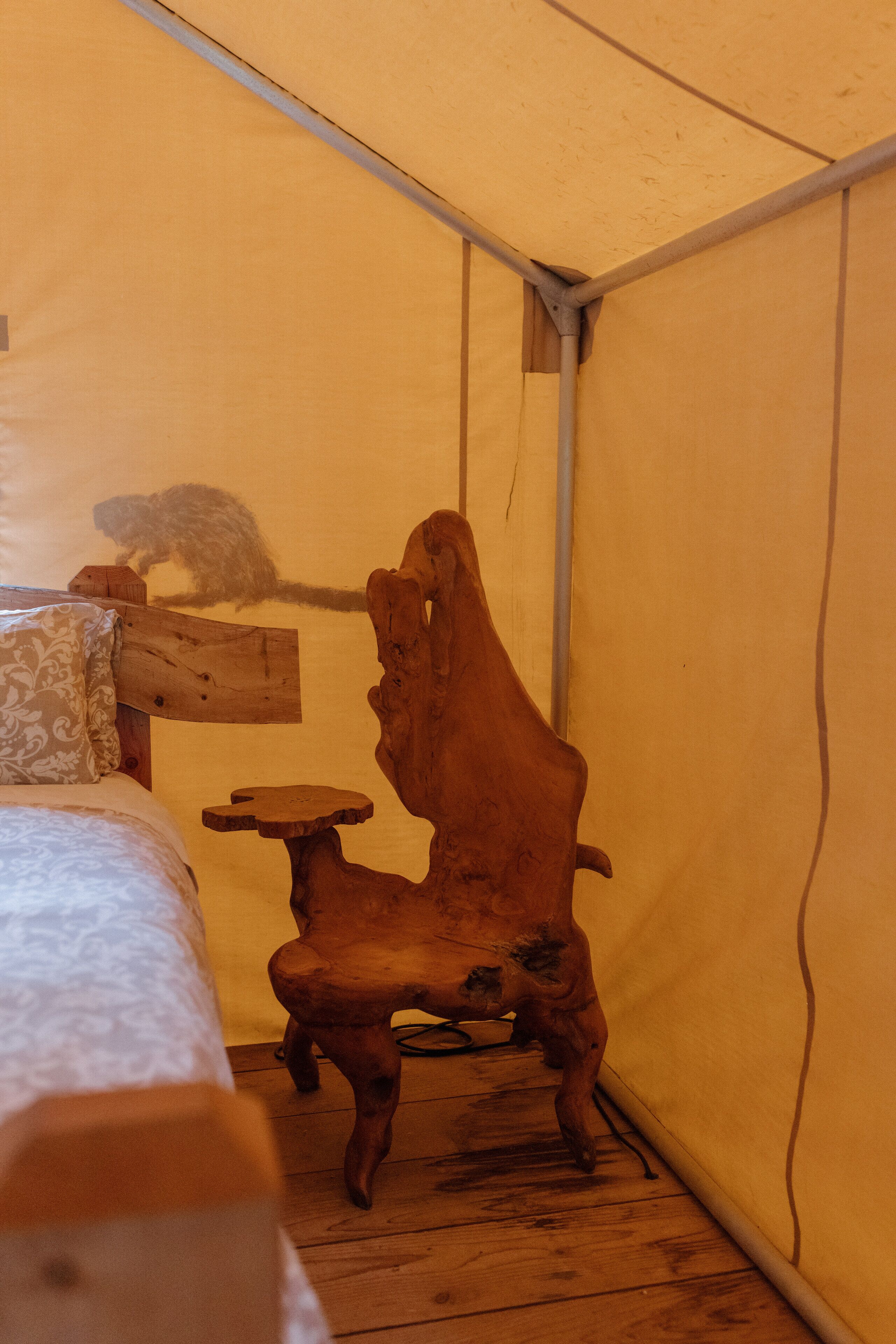 Una tienda de campaña con una cama, una silla de madera y una mesita.