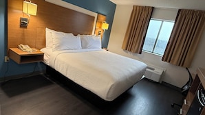 Habitación de hotel con cama, lámparas de noche, teléfono, ventana con cortinas y aire acondicionado instalado en la pared.
