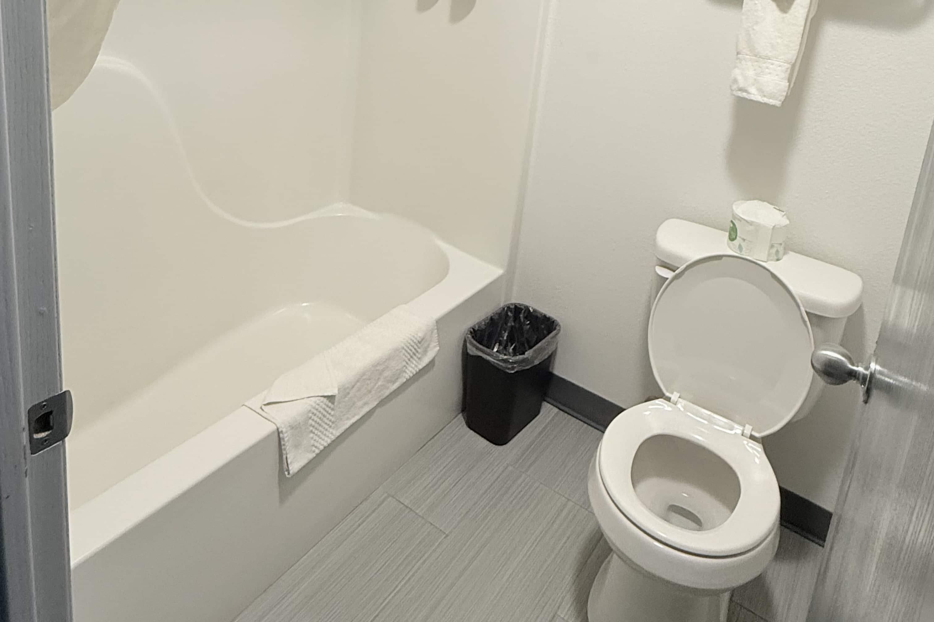A bathroom with a bathtub, toilet, and trash can.