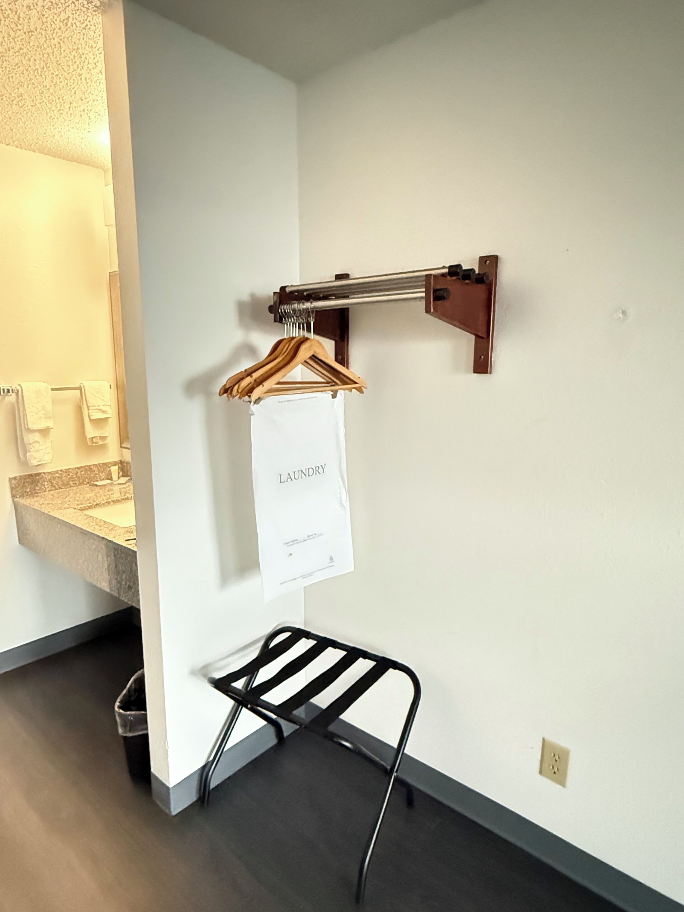 A bathroom with a towel rack, a hanging paper labeled 'laundry,' and a black metal drying rack.
