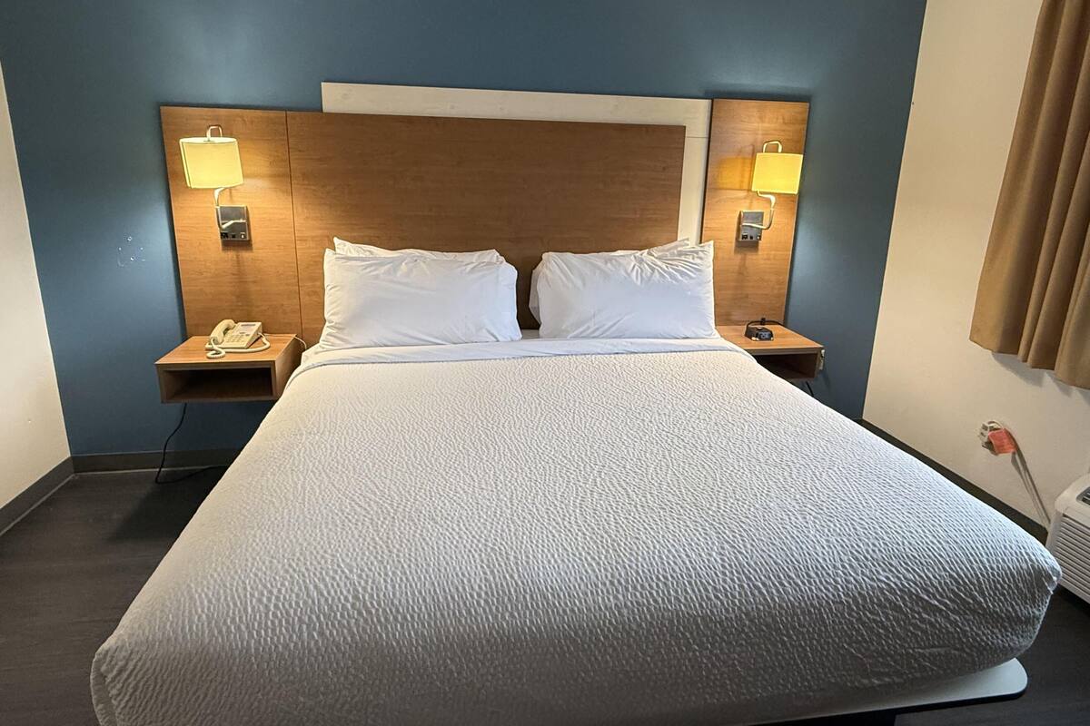 Una habitación de hotel con una cama grande, dos mesitas de noche con lámparas, un teléfono y un aire acondicionado instalado en la pared.