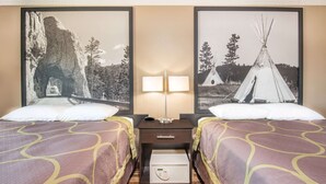Hotelkamer met twee bedden, een nachtkastje met een lamp, een kluis, en prenten van een rotsboog en een tipi.