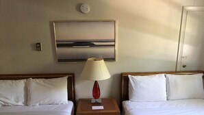 A hotel room with two beds, a nightstand with a lamp, a painting on the wall, and a door. - Atlantic Breeze Inn (Old Orchard Beach)
