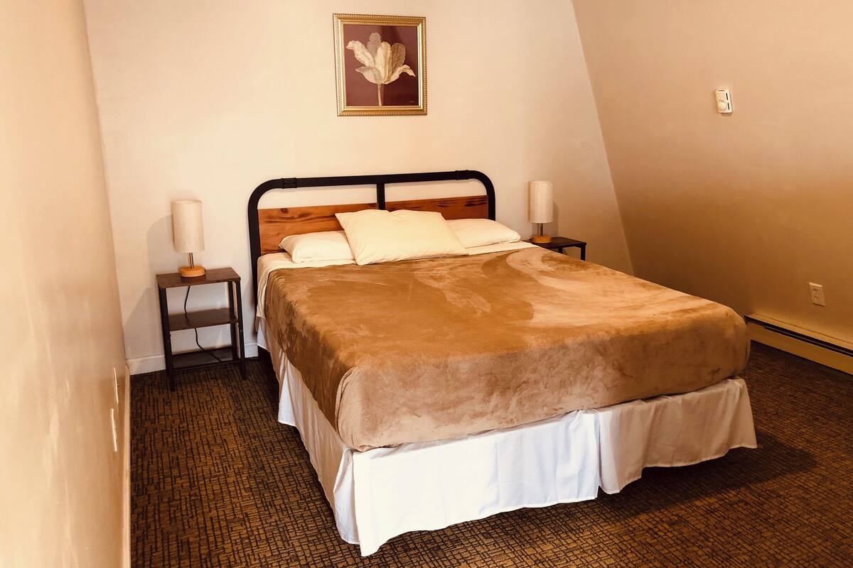 A neatly made bed with a brown blanket, a wooden headboard, and two bedside lamps.