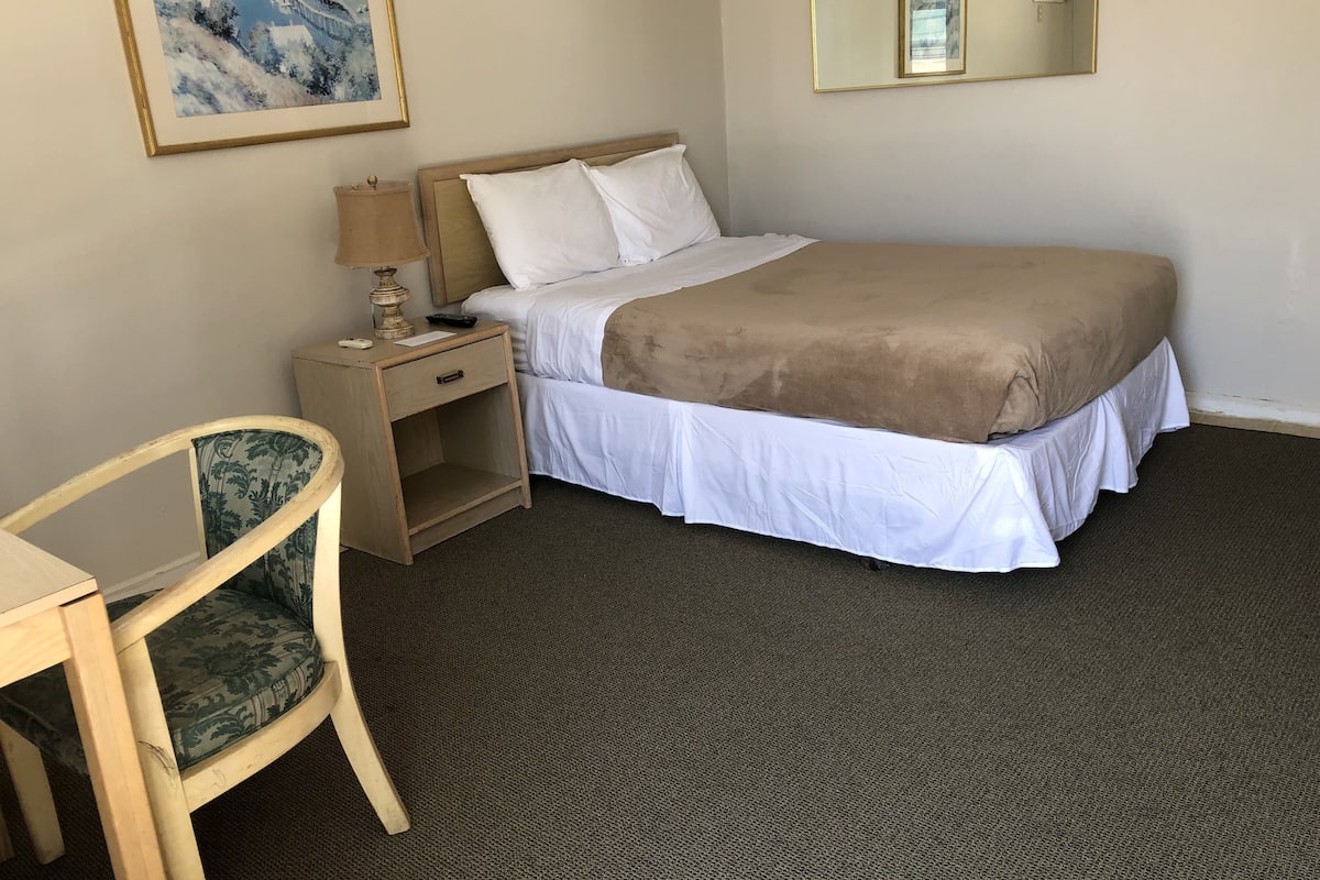 A hotel room with a bed, a nightstand, a chair, a lamp, a painting, and a mirror.