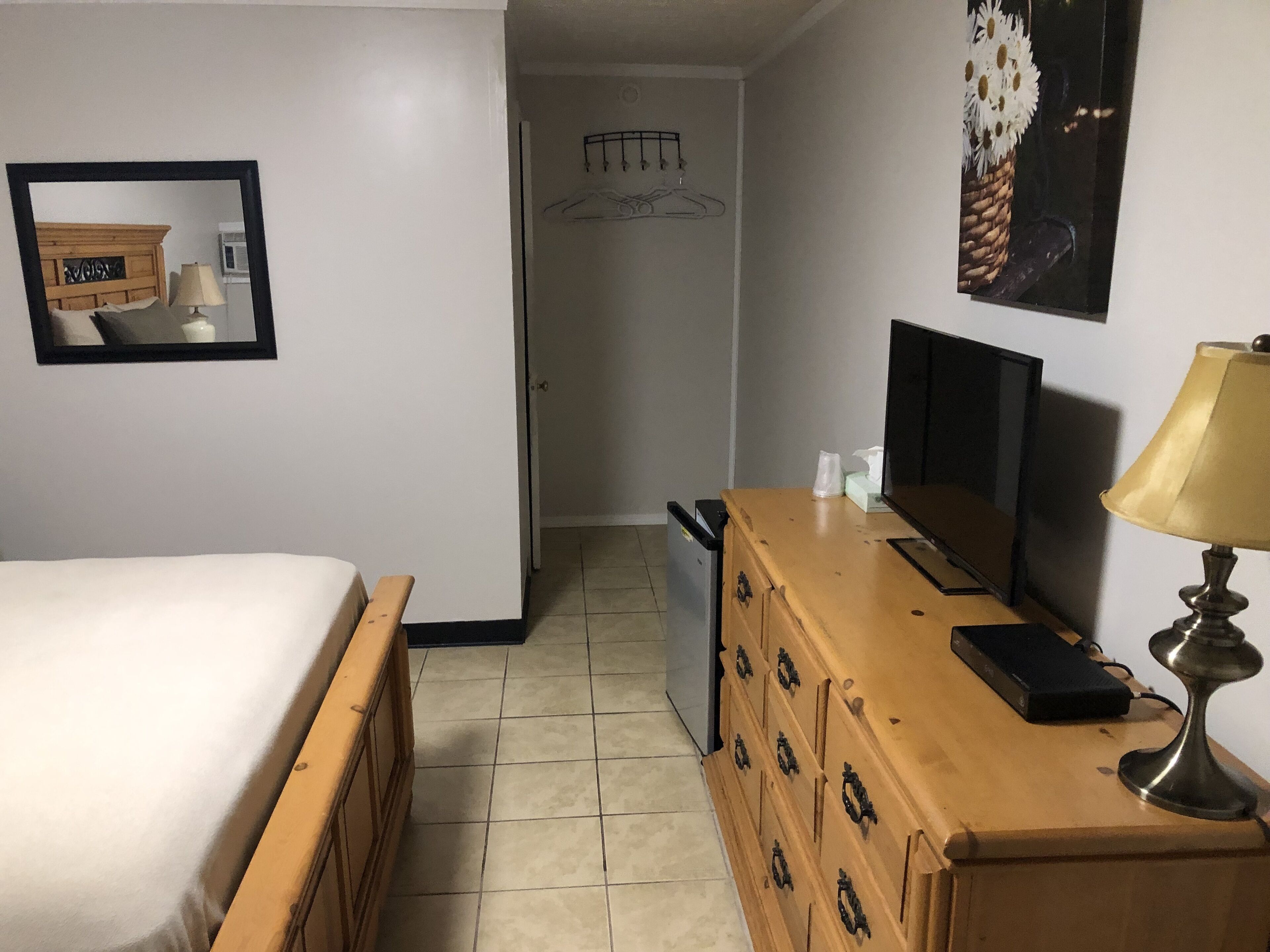 A hotel room with a bed, a wooden dresser, a television, and a lamp.