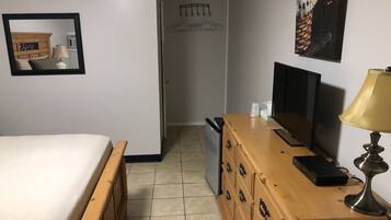 A hotel room with a bed, a wooden dresser, a television, and a lamp.