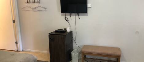 A hotel room with a bed, a small desk with a TV, a bench, and a coat rack.