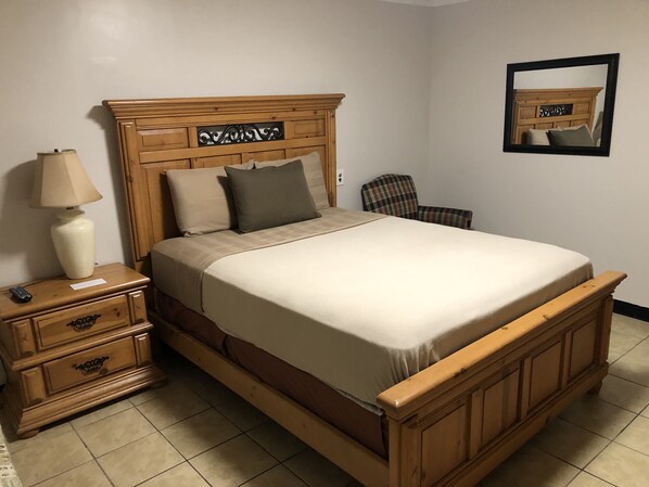 A wooden bed with a headboard, a bedside table with a lamp, and a chair.