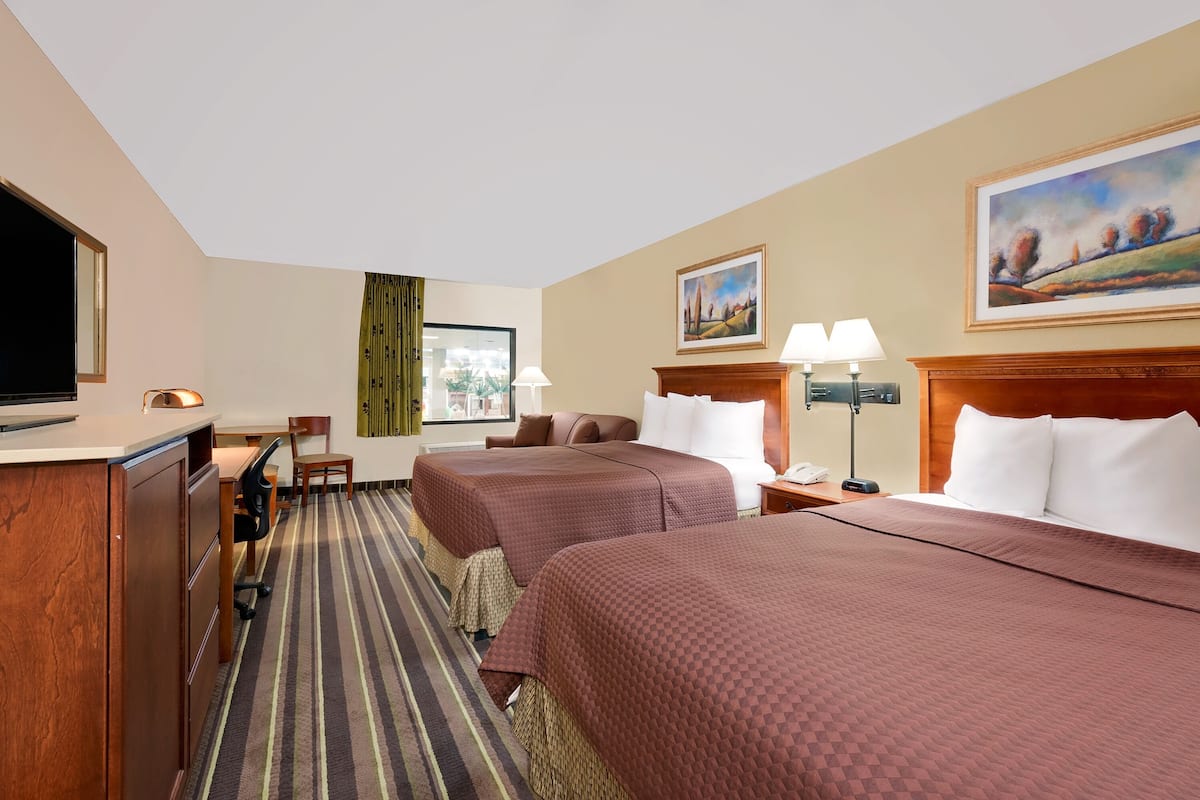 A hotel room with two beds, a desk, a television, and a window with curtains.