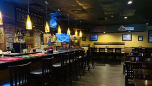 Zona de bar con muebles de madera, luces colgantes y una pantalla de televisión.
