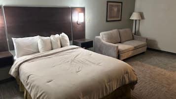 A hotel room with a large bed, a sofa, a nightstand, and a lamp.