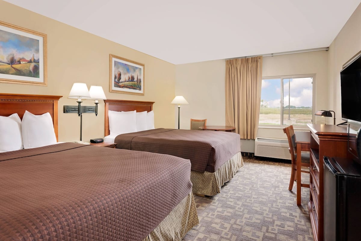A hotel room with two beds, a desk, a chair, a TV, and a window with curtains.