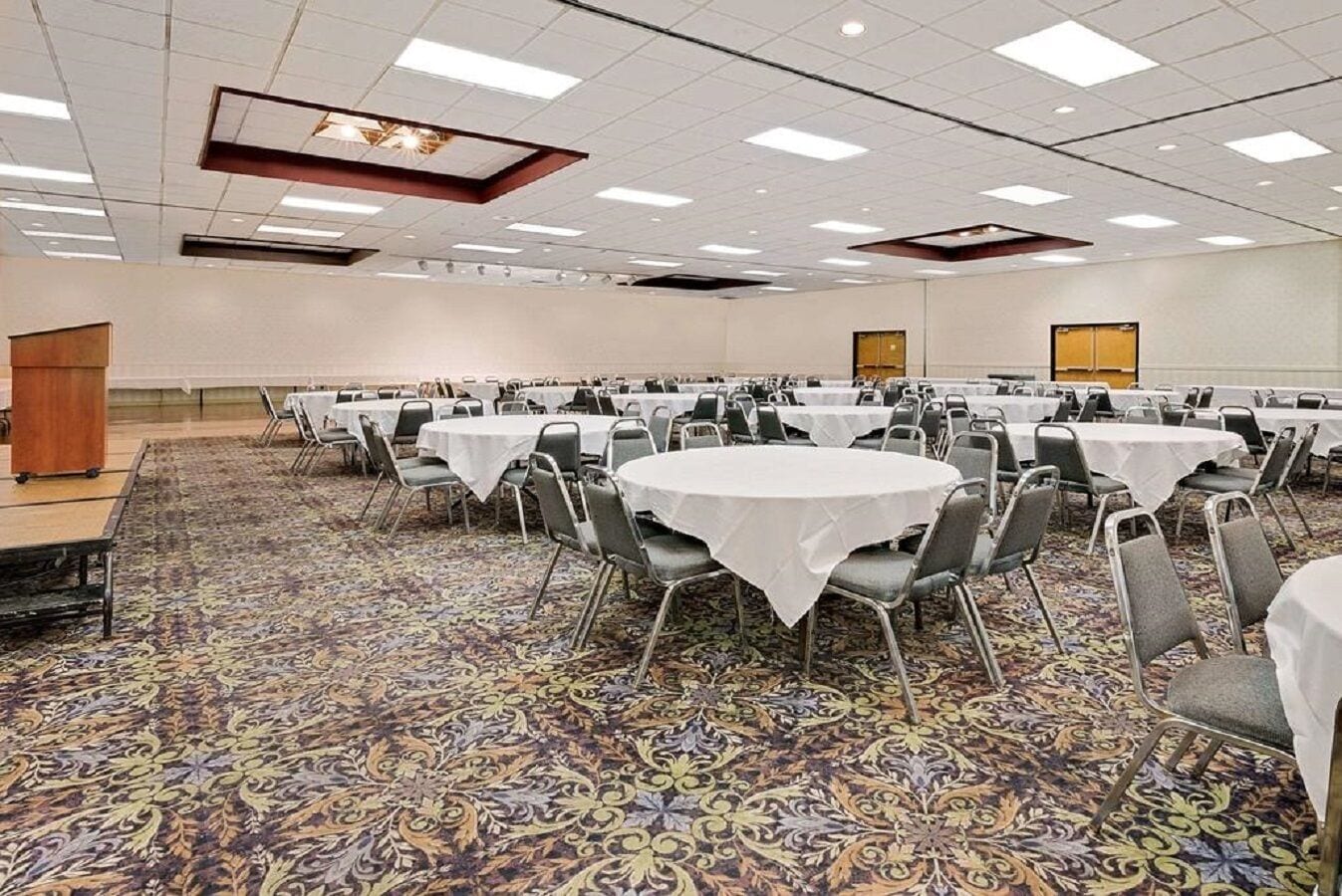 A conference room with round tables and chairs, carpeted floor, and a high ceiling with recessed lighting.