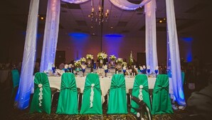 Un salón de banquetes con mesas dispuestas para un evento formal, cubiertas con telas blancas e iluminado por candelabros.