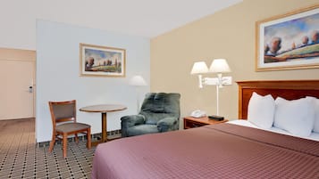 Quarto de hotel com uma cama, uma cadeira, uma mesa e duas pinturas nas paredes.
