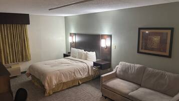 Una habitación de hotel con una cama, un sofá, una mesita de noche, una lámpara de pared y un cuadro enmarcado.