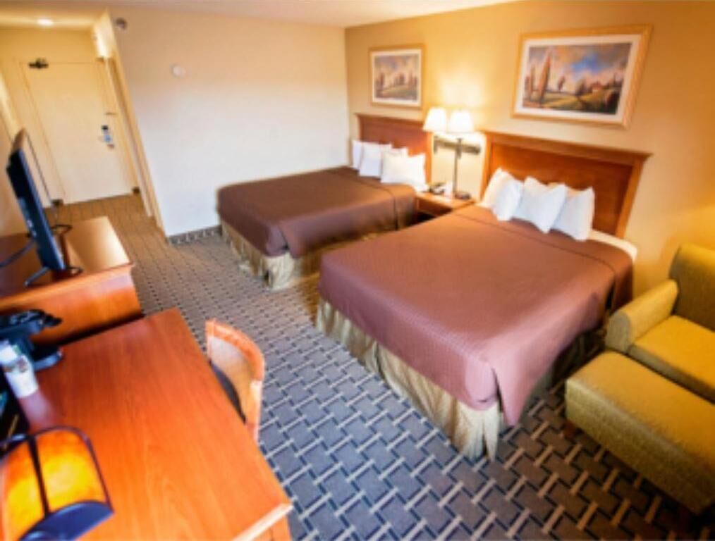 A hotel room with two beds, a desk, a chair, and a television.