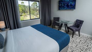 Habitación de hotel con una cama grande, un escritorio con dos sillas, un televisor en la pared y una ventana con cortinas.