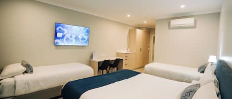 A hotel room with two beds, a desk, a chair, a TV, and an air conditioning unit.