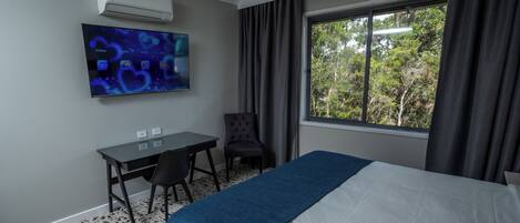 Habitación de hotel con cama, escritorio, silla, televisor montado en la pared y ventana con cortinas.