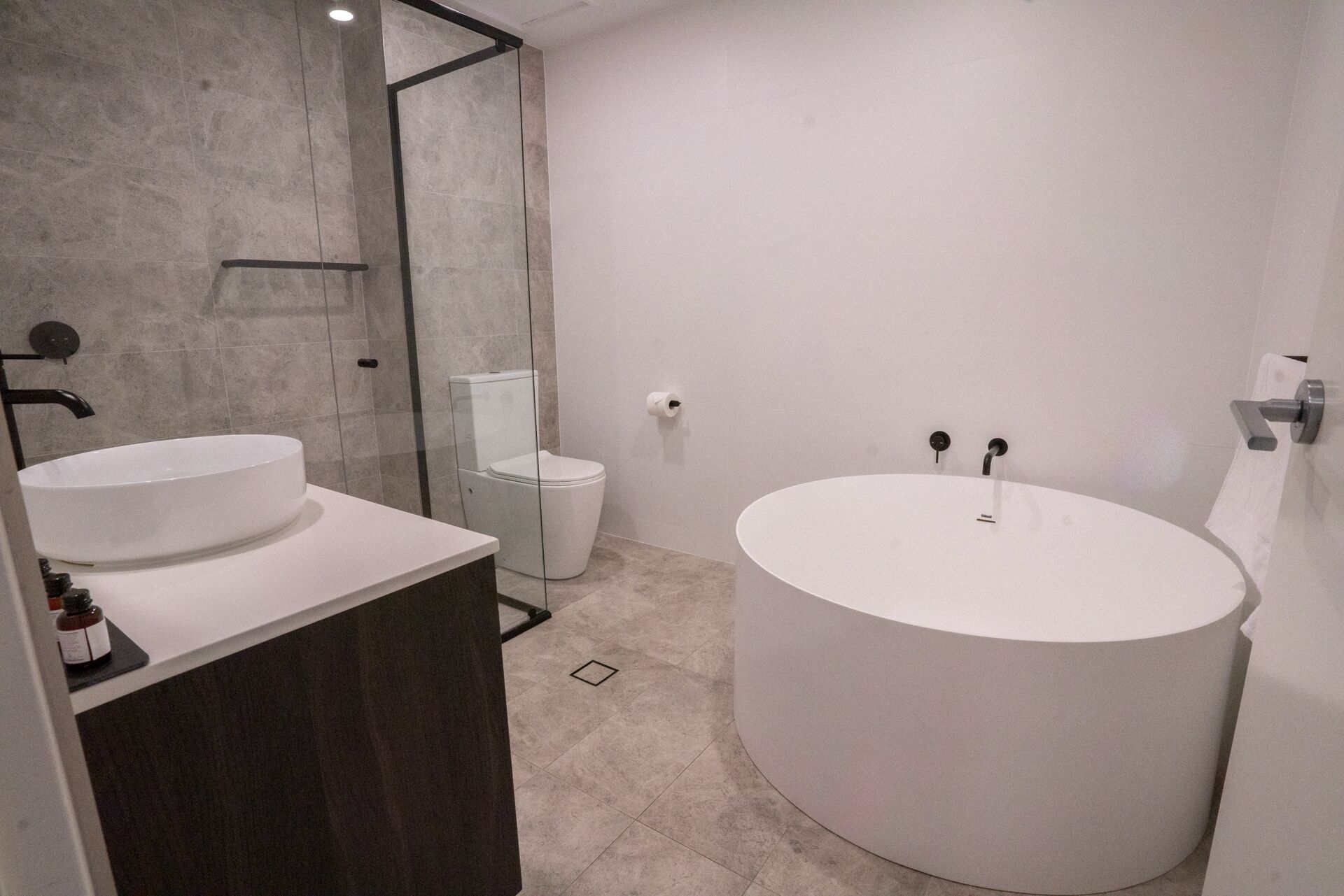 Un baño moderno con un lavabo ovalado grande, un inodoro separado y un box de ducha de vidrio.